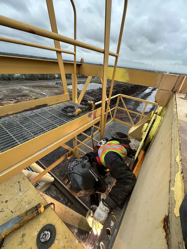 Welder in hi-vis welding heavy steel on an elevated platform