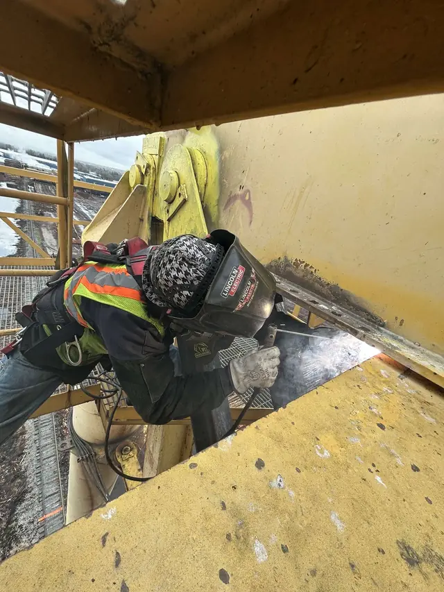 Welder grinding heavy steel on an industrial platform