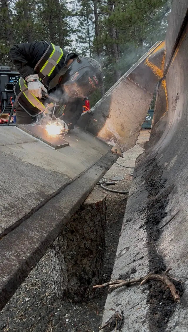 Welder in hi-vis welding a loader bucket repair on site