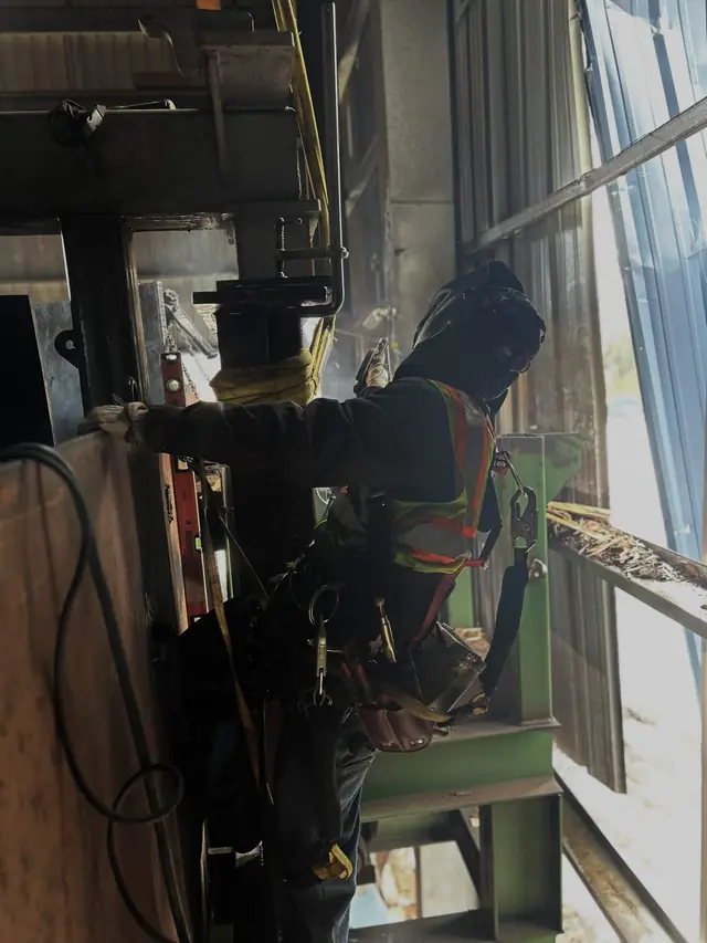 Welder in fall protection repairing a plant frame