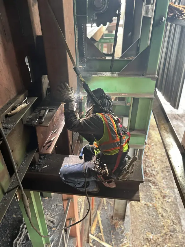 Welder in a fall-protection harness welding industrial machinery