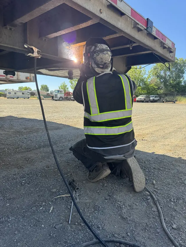 Welder under a semi flatbed trailer welding a cracked I-beam in Redding