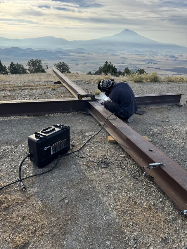 AHT welder welding a heavy steel beam on a hilltop job site with Mt. Shasta behind