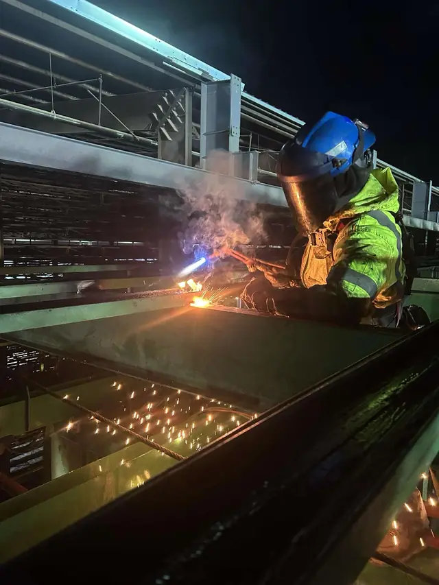 Welder in hi-vis welding heavy steel at night